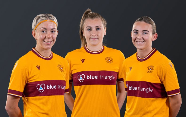 Three young women wear Motherwell Football strips, featuring the Blue Triangle logo.