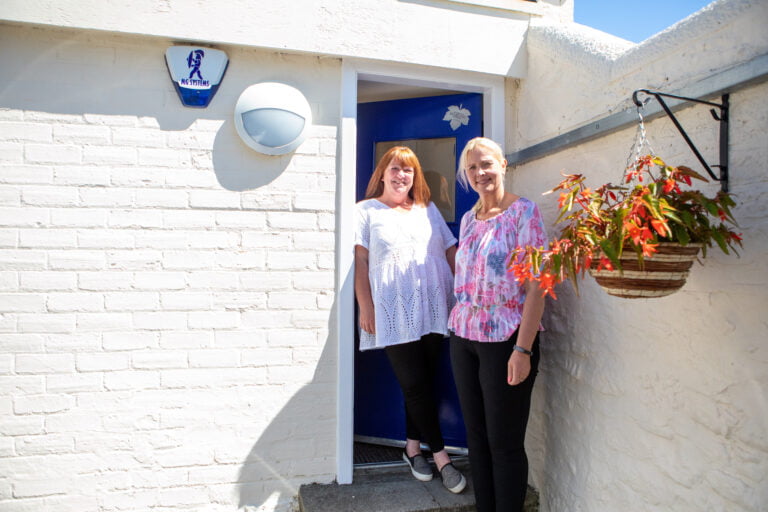 Two female staff members stand outside a door in the sun.