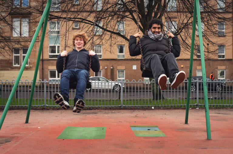 Two young men on swings in a park