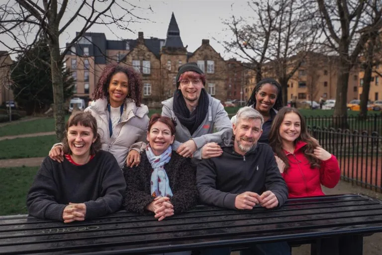 Group of people sit at a bench outside in a a park