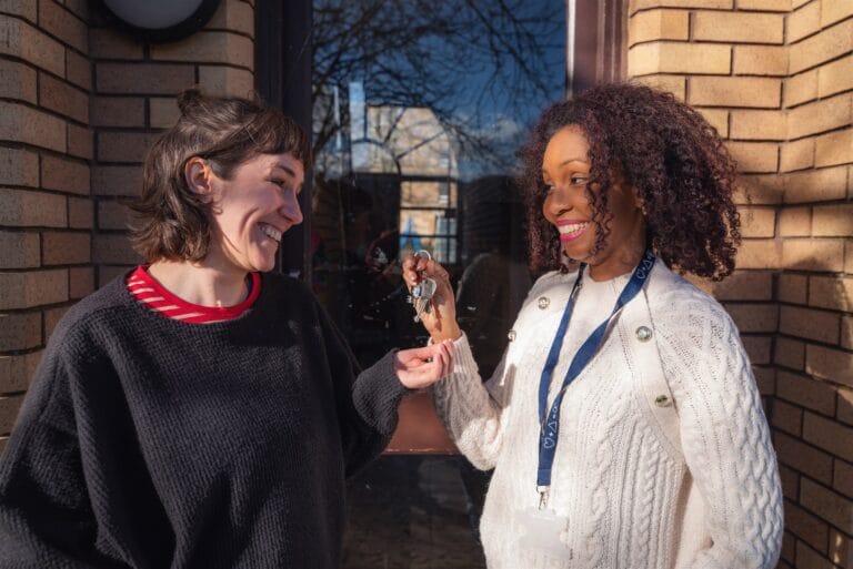 Blue Triangle worker hands a set of keys to a supported person outside a flat door
