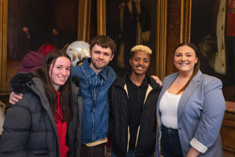 Four people in a group facing the camera, looking happy and relaxed.