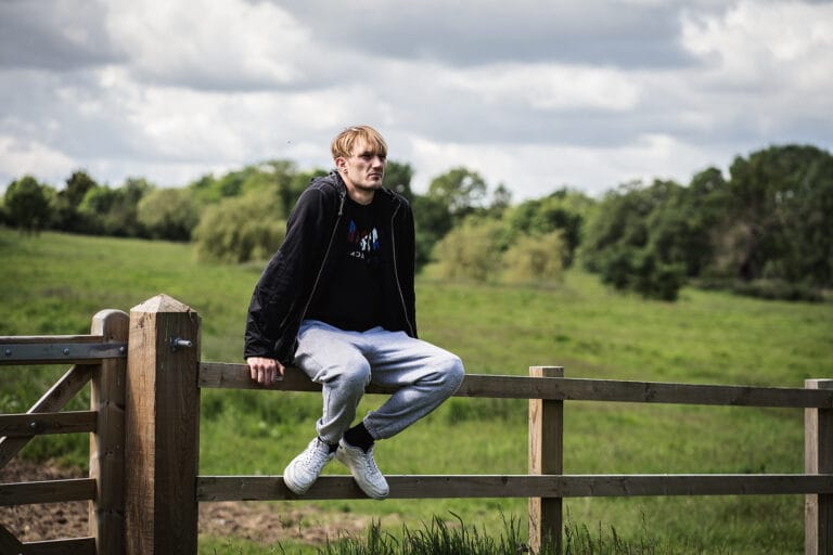 Person looking to the side, looking pensive and deep in thought, sitting on a fence in the countryside.