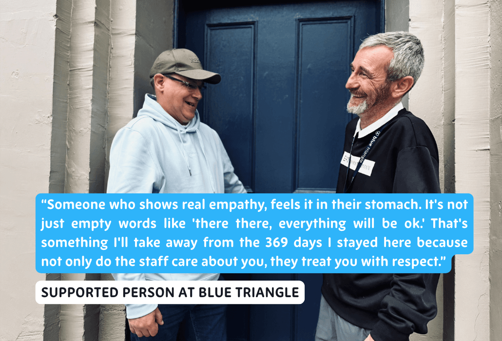 Two people standing at a blue front door, looking at each other and laughing.