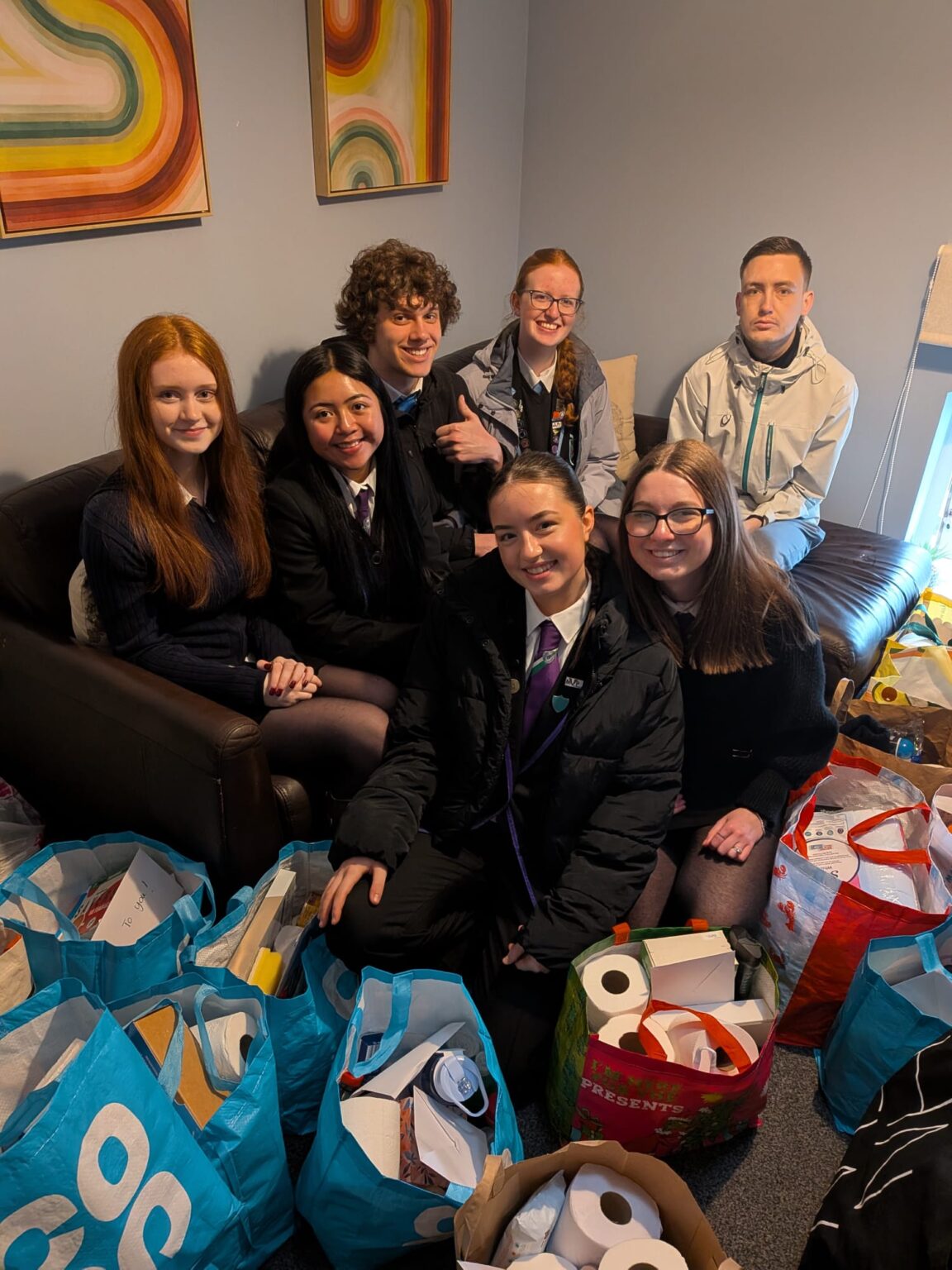 1Mark Scott Award pupils delivering welcome packs to Blue Triangle, surrounded by shopping bags filled with toiletries and household essentials.